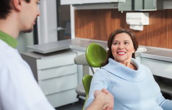 A dentist shaking hands with a woman patient sitting in a dental chair.