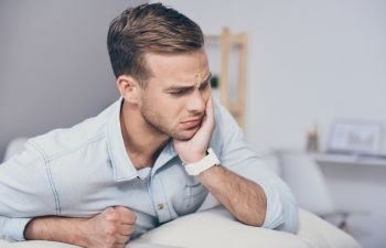 A young man with severe dental pain touching his jaw.