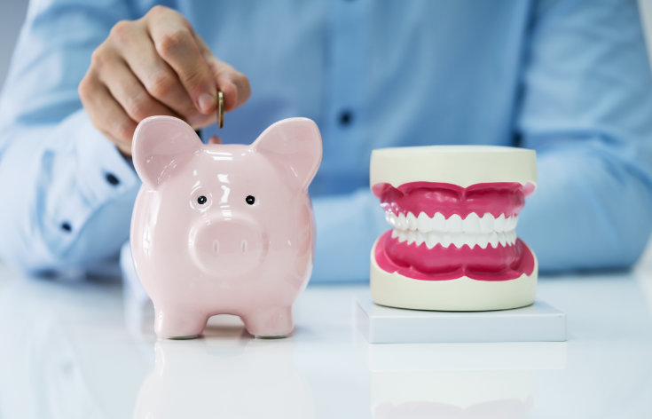 a man saving a coin in a money bank standing next to a dental model