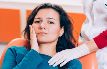 A woman with jaw pain sitting in a dentist's chair during a dental appointment.