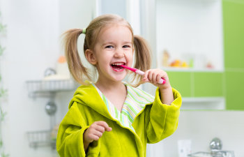 A little girl brushing her teeth in the bathroom.