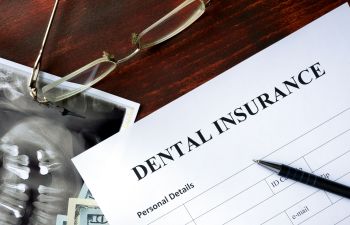 A dental insurance form on a table with glasses and money.