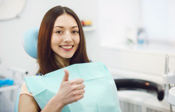 A woman giving a thumbs up while sitting in a dentist's chair.