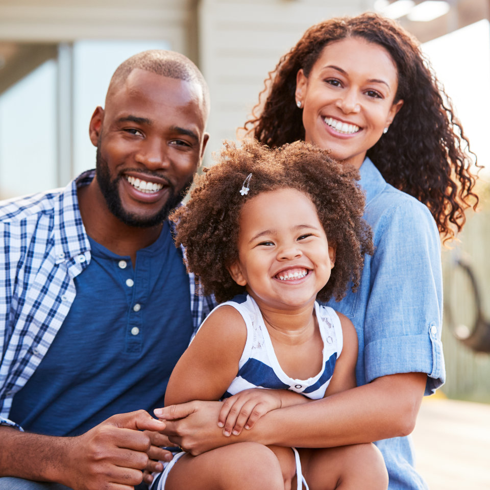 An african-american man and woman smiling with their daughter on a porch.