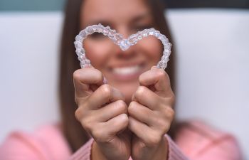 Woman With Perfect Smile After teeth straightening with clear aligners holding the aligners put in the shape of heart in front of her face