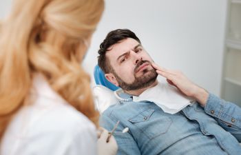 concerned man with dental pain sitting in a dental chair before infected teeth treatment
