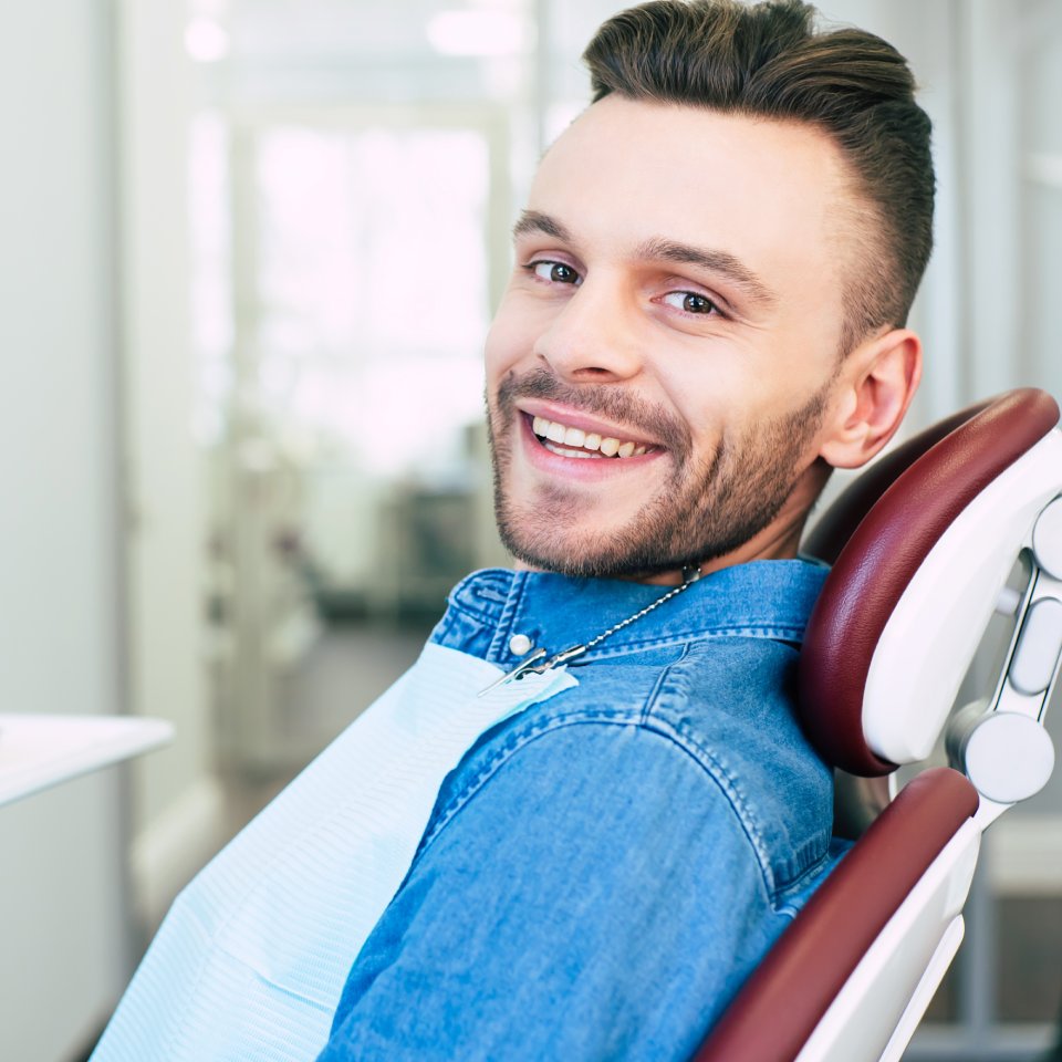 Happy man with hazel eyes and dark brown hair is sitting in dental chair