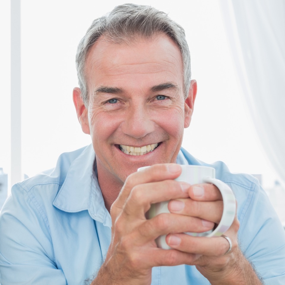 A smiling man in a blue shirt with cup of tea.
