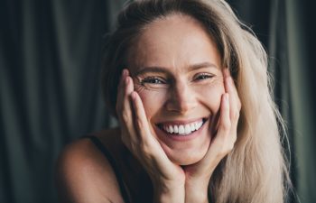 No filter studio photo of pretty shiny woman wear lingerie arms cheeks enjoying self acceptance isolated khaki cloth background
